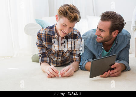 Happy homosexual couple lying on floor and using tablet computer Stock Photo