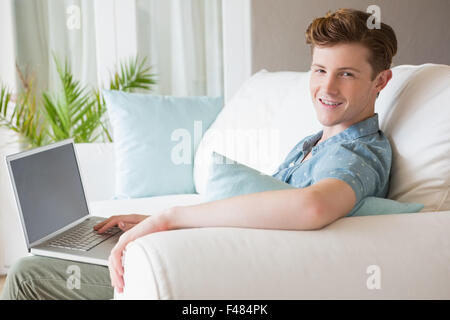 Happy young man smiling at camera and using laptop on couch Stock Photo