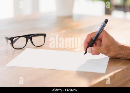 Side view of hand writing on white page on working desk Stock Photo