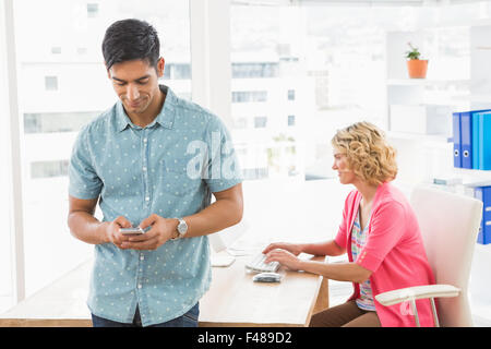 Smiling man posing in front of his colleague using smartphone Stock Photo
