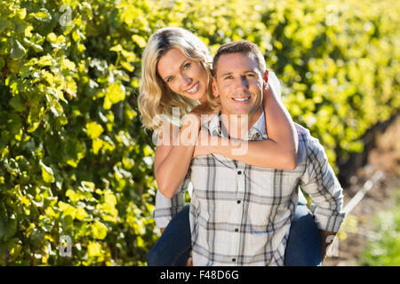 Portrait of smiling man giving his woman a piggyback next to grapevine Stock Photo