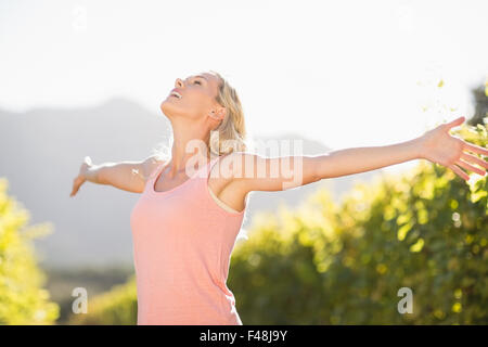 Smiling blonde woman standing in front of grapevine with eyes closed and arms outstretched Stock Photo