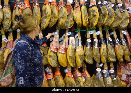 Woman shopper shopping buying Cured hams Jamon Iberico iberian Ham Hanging in Spain Spanish supermarket Stock Photo