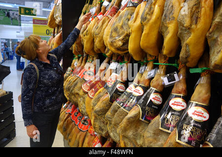 Woman shopper shopping buying Cured hams Jamon Iberico iberian Ham Hanging in Spain Spanish supermarket Stock Photo