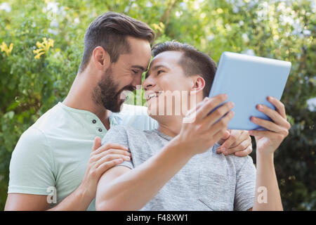 Happy homosexual couple using tablet and hugging Stock Photo