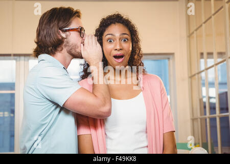 Businessman whispering into female colleague ear Stock Photo