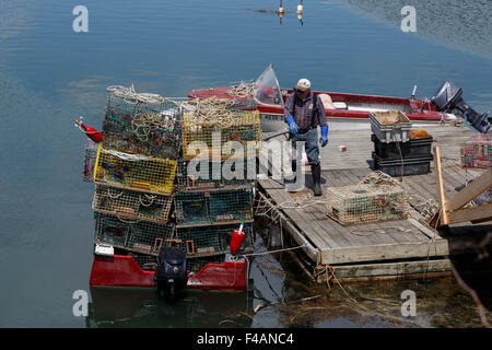 Fisherman loading lobster pots on to small boat from a floating wooden dock Harpswell Sound Maine USA Stock Photo