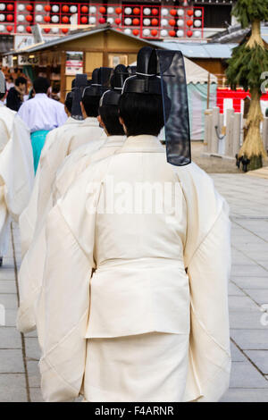 Nishinomiya shrine, Japan, Shinto Priest ceremony, priests, kannushi, walking away in line, all wearing Kammuri, black hats. View from behind. Stock Photo