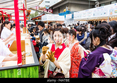 Ikuta Shinto shrine, Japan, during Shogatsu, new year. Three young women wearing kinmono, buying omikuji, fortune paper, from Miko, shrine maiden. Stock Photo