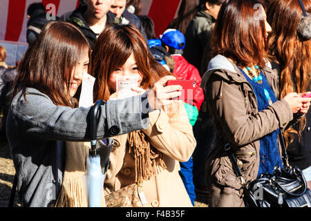 Kyoto, Yasaka shrine, New Year's day, Shogatsu. Two young women, smiling, taking picture, selfie, with mobile phone during their Hatsumode visit. Stock Photo