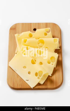 thin slices of emmental cheese on wooden cutting board Stock Photo