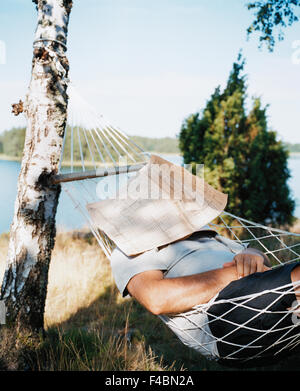 It is located in the hammock with a newspaper over his face. Stock Photo