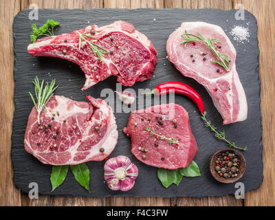 Raw meat steaks with spices on the black cutting board. Stock Photo