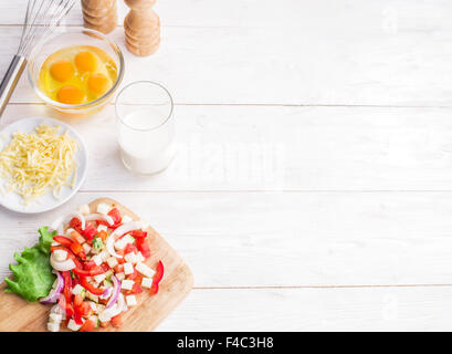 Omelet ingredients: eggs, fresh cut vegetables, milk and cheese on the wooden table. Stock Photo