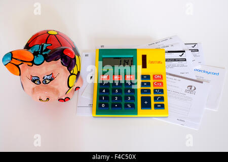 pile of unpaid bills and calculator with piggy bank looking on against a white background england uk Stock Photo