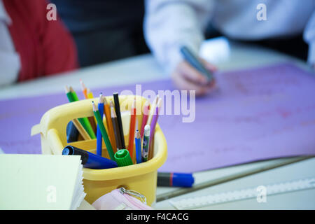 A typical UK primary school classroom with coloured pencils in the foreground and pupils in the background Stock Photo