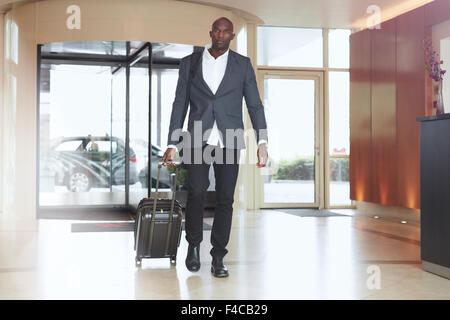 Businessman walking in hotel lobby. Full length portrait of young african executive with a suitcase. Stock Photo