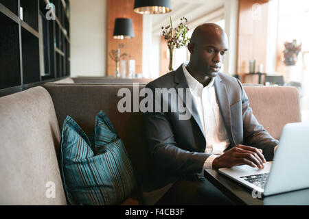 Image of young man sitting at cafe working on laptop. African businessman at coffee shop surfing internet on laptop. Stock Photo