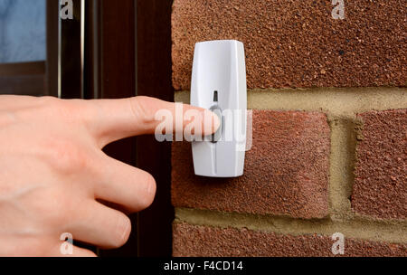 Close-up of woman pressing the button of a doorbell on a brick wall Stock Photo