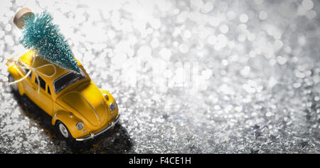 Miniature yellow car with fir tree on silver background Stock Photo