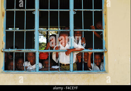 Tanzania, Mwanza, children looking and smiling through a grid window of school Stock Photo