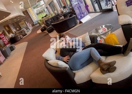 couple smooch on a sofa at dfs store GV's retail units and shoppers at Forster Square Retail Park, Bradford. A British Land PLC retail property. Stock Photo