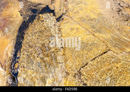 Clear shallow stream seen from above. Abstract view of water flowing over golden rock with ripples reflecting sunlight, England, UK Stock Photo