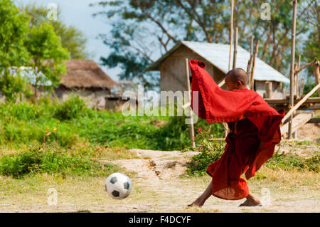 Monk in red robe playing football Stock Photo