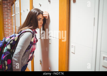 Upset female student leaning on locker Stock Photo