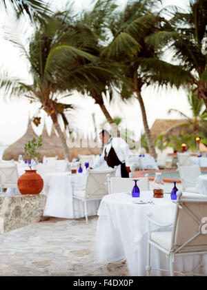 A Mexican waiter sets a table at an outdoor oceanside restaurant at Maroma Spa and Resort. Maroma is a luxury resort located in Stock Photo