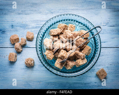 Cane sugar cubes in the old-fashioned glass plate on blue wooden table. Stock Photo