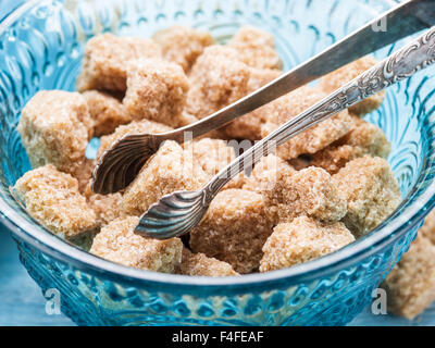 Cane sugar cubes in the old-fashioned glass plate and sugar tongs. Stock Photo