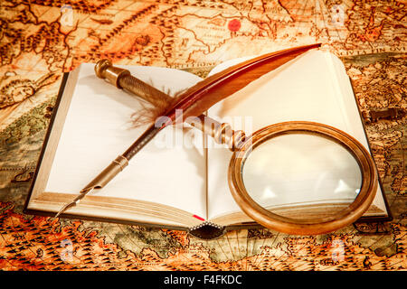 Vintage still life - magnifying glass, old book and goose quill pen lying on an old map in 1565. Stock Photo