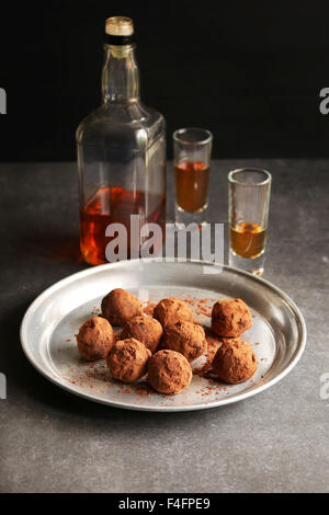Chocolate truffles on an aluminum plate with 2 glasses of liqueur and a bottle on background Stock Photo