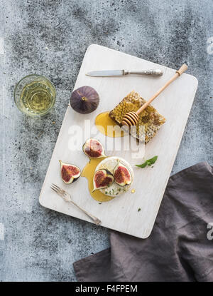 Camembert cheese with fresh figs, honeycomb and glass of white wine on serving board over grunge rustic grey backdrop, top view Stock Photo
