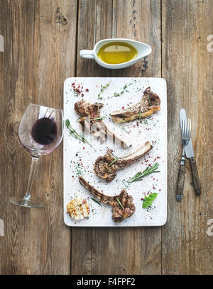 Grilled lamb chops. Rack of Lamb with garlic, rosemary and spices on white serving board, wine glass, oil in a saucer, dinnerwar Stock Photo