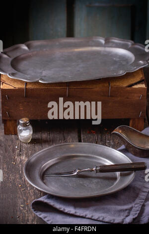 Table Setting with Empty vintage metal plate and dish with fork, napkin and salt, prepare for rustic dinner. Over old wooden tab Stock Photo