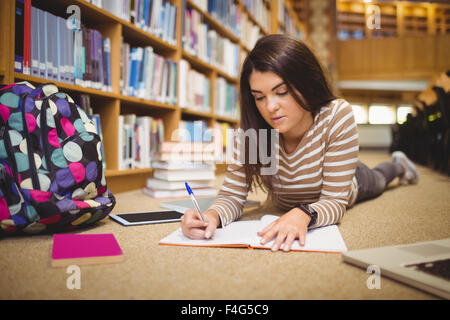 Young beautiful student writing while lying on floor Stock Photo