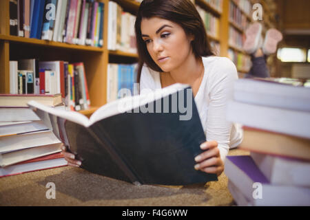 Female student reading book while lying on floor Stock Photo