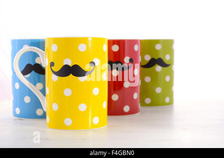 Colorful polka dot coffee mugs with mustaches for November Mens health awareness on white wood table. Stock Photo