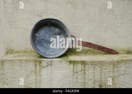 Vintage old rusty frying pan against wall. Stock Photo