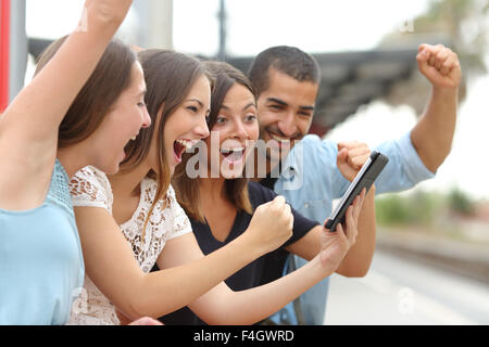Four euphoric multi ethnic caucasian and arab friends watching tv on a a tablet in a train station