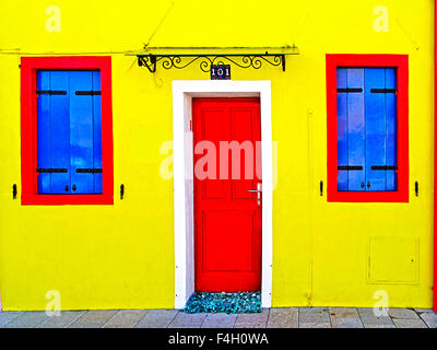 BURANO, ITALY- yellow house with blue shutters and red wooden door Stock Photo