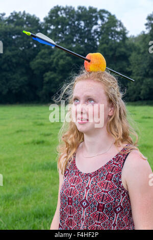 Young woman looking afraid at arrow in apple on head outdoors Stock Photo