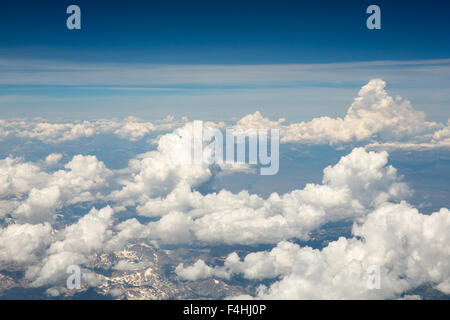 Fluffy white clouds viewed from an airplane.  Snow-covered Rocky Mountains can be seen through the clouds.  Copy space. Stock Photo