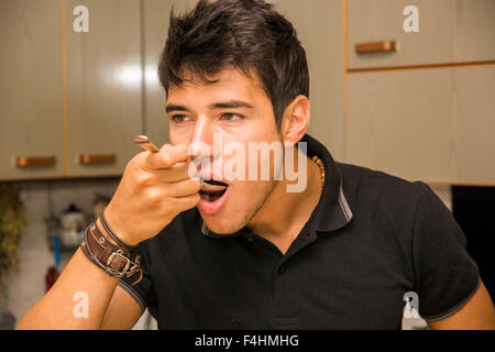 Sick handsome young man taking cough syrup or medication from spoon, in home kitchen Stock Photo
