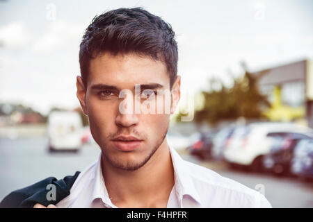 Headshot of handsome young man with white shirt in city street, lit by sunset light, looking at camera Stock Photo