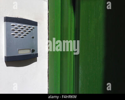 Old intercom over whitewashed wall, beside green wooden door Stock Photo