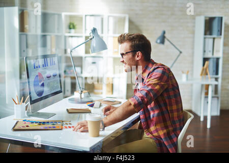 Young man looking at electronic document with financial data shown in diagrams Stock Photo