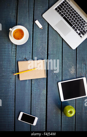 Technological devices, cup of tea, green apple and notebook with pencil on wooden table Stock Photo